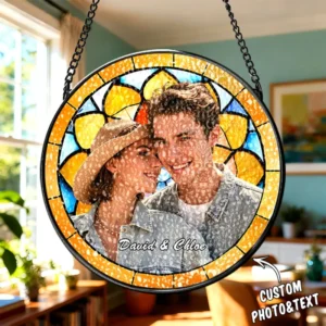 Round hanging custom photo plaque with stained-glass-style border in yellow and blue tones, suspended by black chains. The center features a smiling couple labeled “David & Chloe,” with a textured overlay effect across the image. The setting appears indoors with warm natural light, and a “CUSTOM PHOTO&TEXT” label with an arrow indicates personalization.