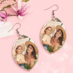6acca181fc684e9a41764886cba702b4webp - printshop4me.ae Pair of teardrop-shaped personalized photo earrings with silver hooks displayed on a pink floral background. Each earring features a custom printed photo of a smiling mother wearing a straw hat holding a young child outdoors, designed as matching photo memory jewelry gifts.