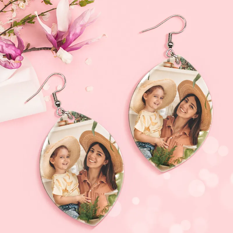 6acca181fc684e9a41764886cba702b4webp - printshop4me.ae Pair of teardrop-shaped personalized photo earrings with silver hooks displayed on a pink floral background. Each earring features a custom printed photo of a smiling mother wearing a straw hat holding a young child outdoors, designed as matching photo memory jewelry gifts.