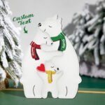A personalized winter-themed wooden decoration featuring a white polar bear family illustration. Two larger bears embrace at the top wearing scarves labeled with names, while a smaller cub sits below holding a red heart. The design includes “Custom Text” indicating personalization options, set against a snowy forest background, suggesting a cozy family-themed gift.