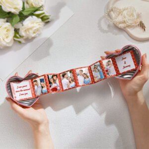 Heart-shaped personalized photo keepsake held in two hands, featuring an accordion-style strip of couple photos with romantic red polka-dot design. The design includes custom text such as “Jane & Jeremy” and a love message, making it a sentimental Valentine’s or anniversary gift for couples.