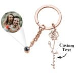 Personalized projection photo keychain in a rose gold finish, featuring a custom engraved rose with name charm and a hidden photo projection lens. Displayed with a sample projected couple photo, this elegant keychain makes a meaningful gift for anniversaries, Valentine's Day, birthdays, weddings, or special occasions.