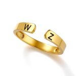 Gold open cuff ring with a polished finish, featuring engraved black initials “W” on one end and “Z” on the other. The adjustable ring has a minimalist curved design and is displayed on a clean white background.