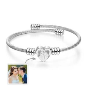 Silver twisted cable-style bracelet with a central heart-shaped charm featuring an engraved couple photo. The bracelet includes adjustable metal bead accents and is displayed on a clean white background, with a small reference image of the original couple photo shown in the bottom left corner.