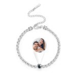 A silver personalized bracelet featuring a circular diamond-studded band and a projection-style photo charm in the center showing a smiling couple. The bracelet includes a small adjustable chain and clasp, with a sleek and elegant design suitable for custom photo jewelry gifts.