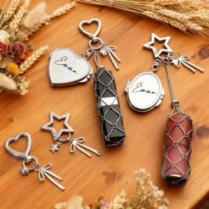 Set of personalized crystal keychains featuring engraved heart and oval lockets with the name "Emma," paired with decorative heart and star key rings, ribbon charms, and wire-wrapped crystal pendants in black and rose quartz. Displayed on a wooden tabletop with dried flowers, these custom name keychains make elegant personalized gifts.