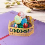 Easter egg basket 3D pop-up greeting card featuring colorful decorated eggs and a cute bunny design inside a yellow basket. A handmade paper pop-up card for Easter celebrations, spring gifting, festive greetings, and seasonal decoration.