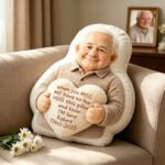 ef4b98d7-24c9-4311-8b34-b9d26bf7619c-0jpeg - printshop4me.ae Personalized memorial photo pillow featuring a cartoon-style elderly man holding a heart cushion with a heartfelt message, displayed on a sofa in a cozy living room setting.
