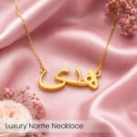 Gold script name necklace on pink satin fabric with small pink flowers, luxury jewelry.