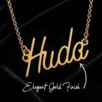 Gold cursive name pendant necklace spelling 'Huda' on a black velvet background with a gold chain guard.